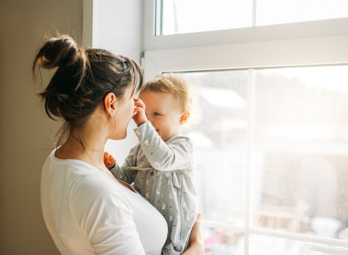  Young woman mom with baby girl on hands near window at home